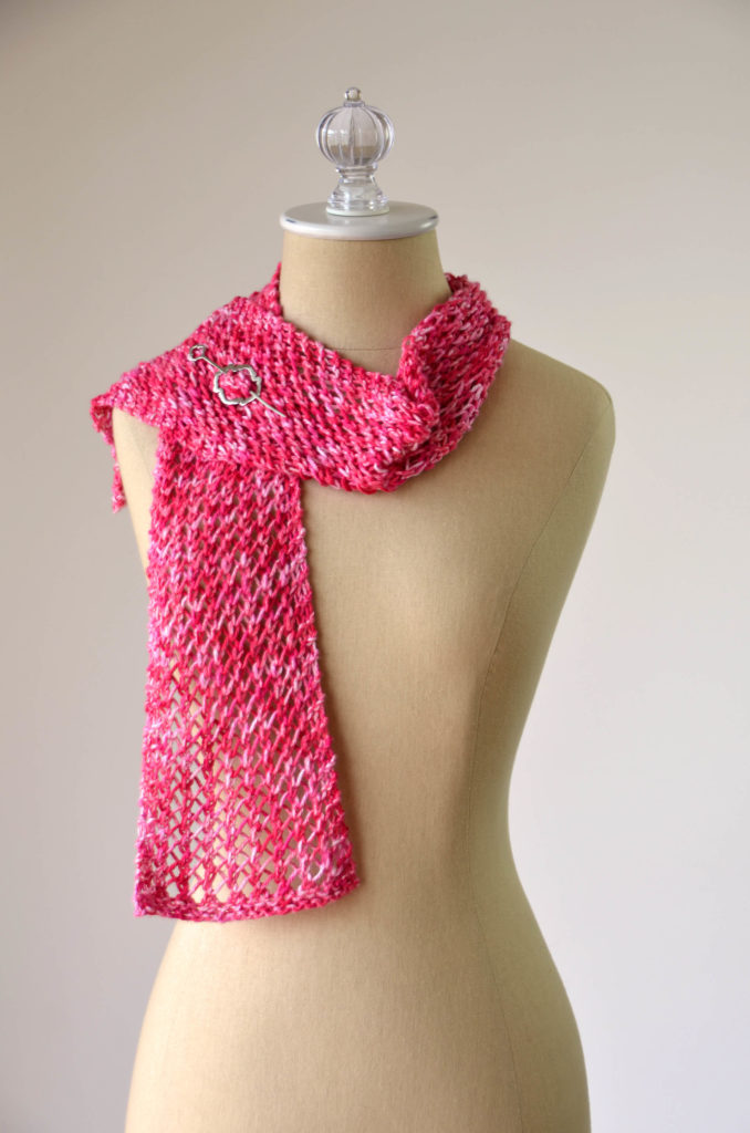 A red lace scarf with one end thrown over the shoulder of a dressform. A silver shawl pin fastens the scarf together.