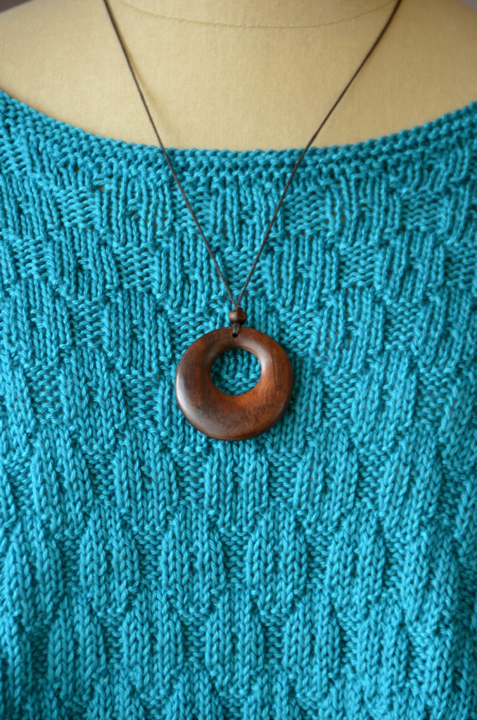 closeup of aqua knitted poncho with wooden necklace