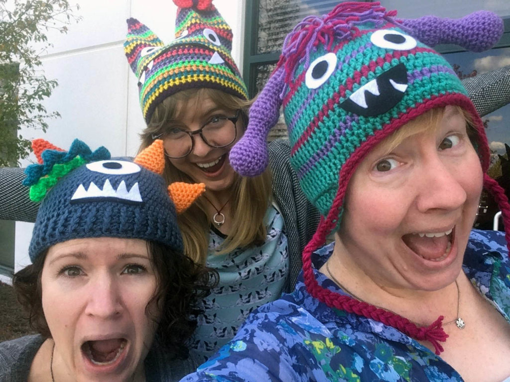selfie of three women wearing colorful crocheted hats with monster faces on them