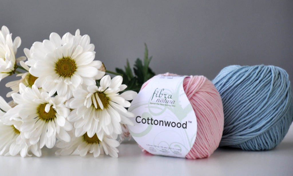 Photo of one pink and one blue ball of Cottonwood yarn next to spray of daisies