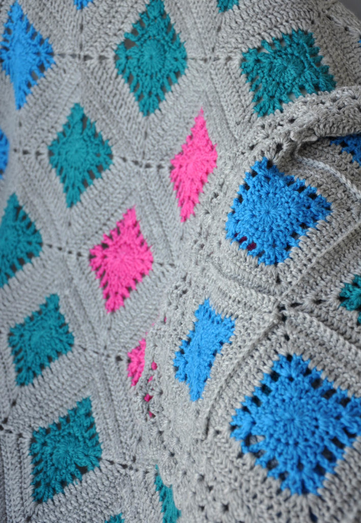 Detail of colored squares in gray crochet background of baby blanket