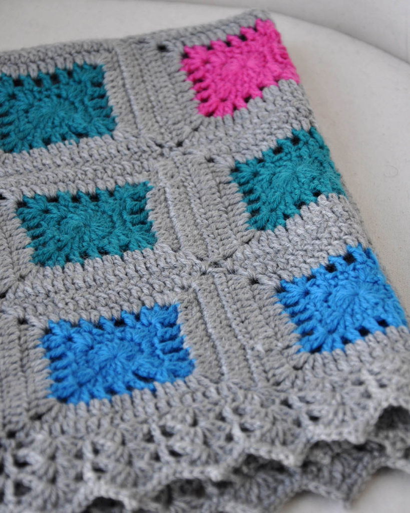 Folded gray, pink, green, and blue blanket crocheted in Oasis with lace border
