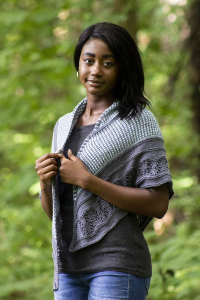 Woman looking at camera while holding edges of her worn Blue Oak Shawl