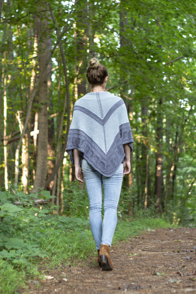 Woman walking away down wooded lane wearing knitted shawl