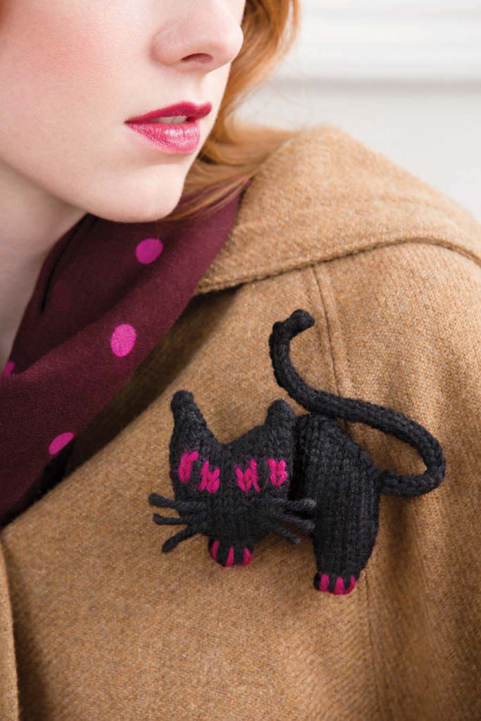 Knitted brooch in the shape of a black cat with hot pink eyes