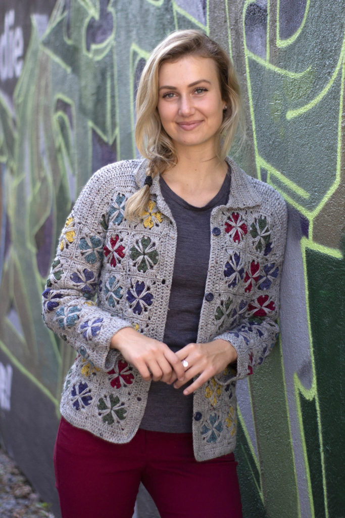 Woman in crocheted jacket leaning against wall