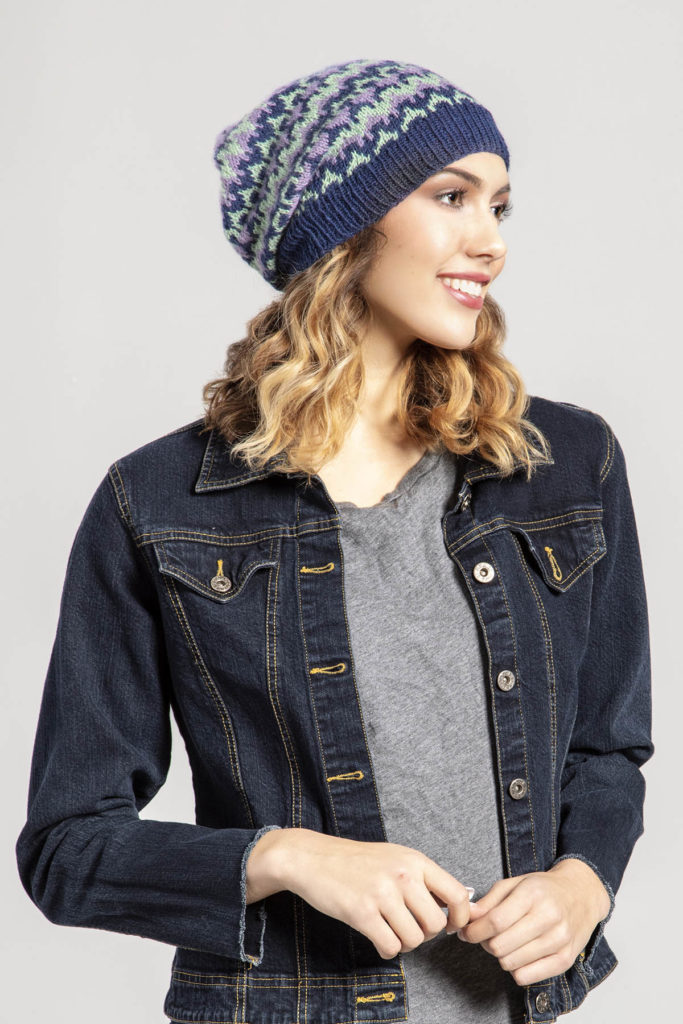 Woman wearing dark blue, sea green, and lavender knitted slouchy cap.