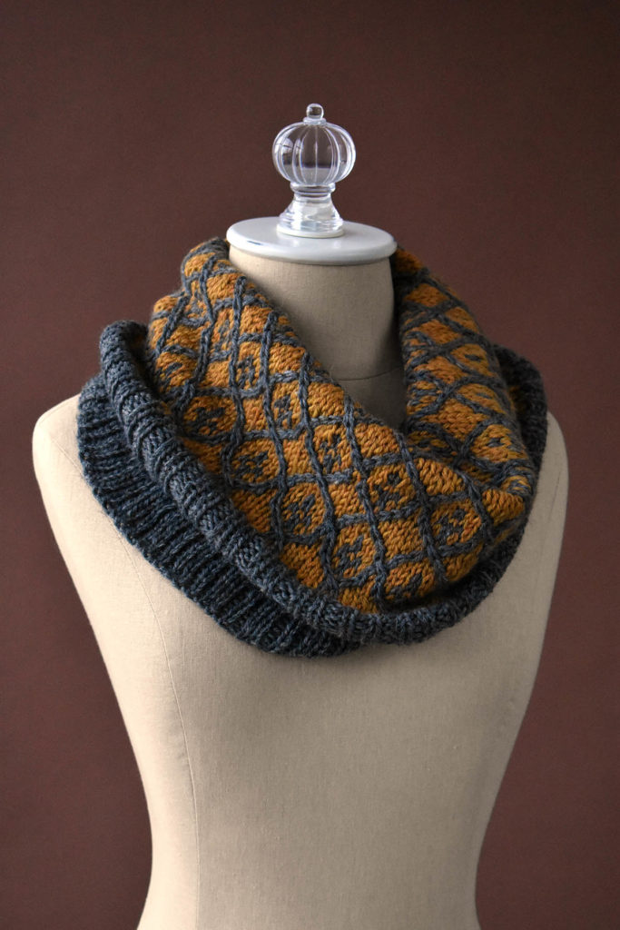 A tan and gray Fair Isle knitted cowl against a brown background.