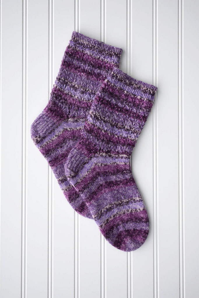 Pair of purple hand-knitted socks against white background