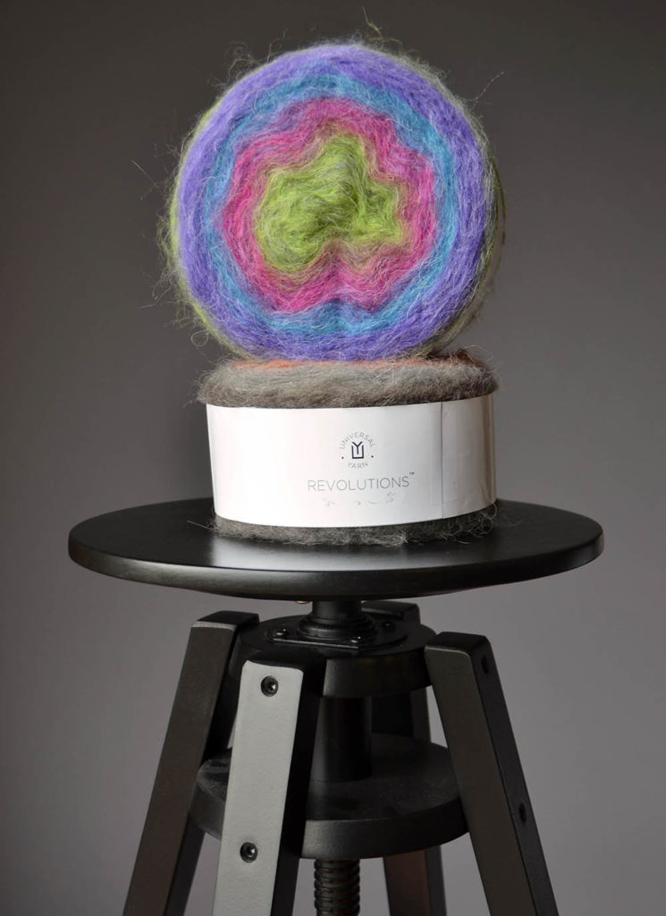 Two cakes of Revolutions yarn on a stool.