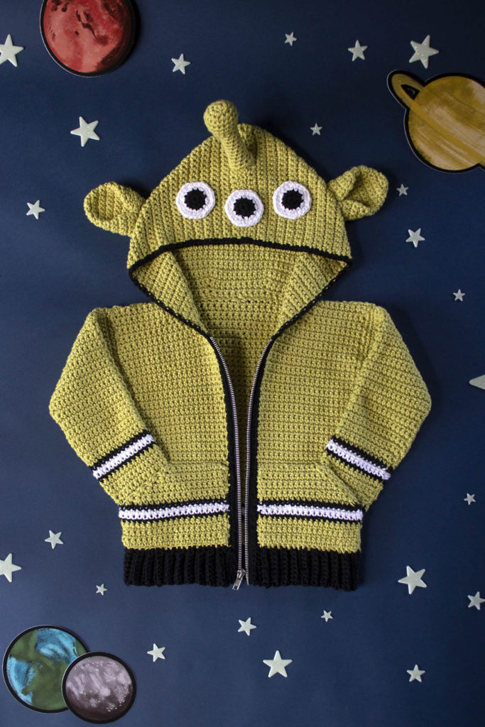 A crochet children's cardigan featuring a fun, alien-themed hood.
