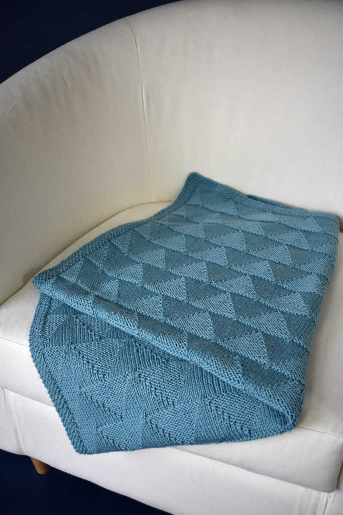 A blue blanket knit in Adore folded on a chair.