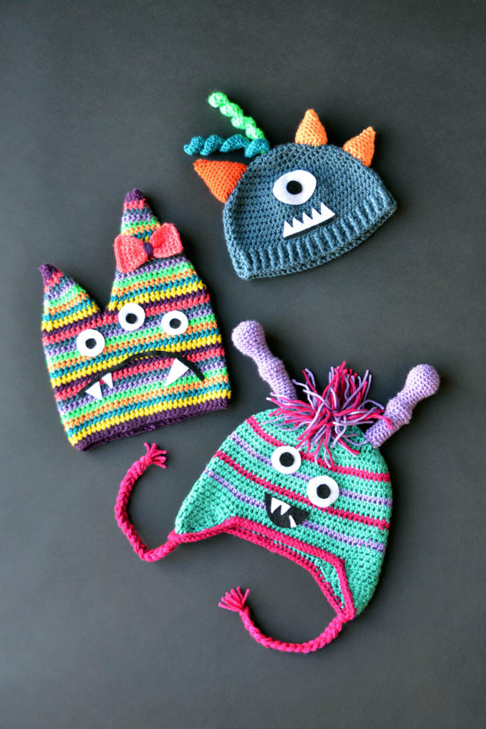 Three brightly colored crochet monster hats in Uptown Worsted pictured laying flat on a table.