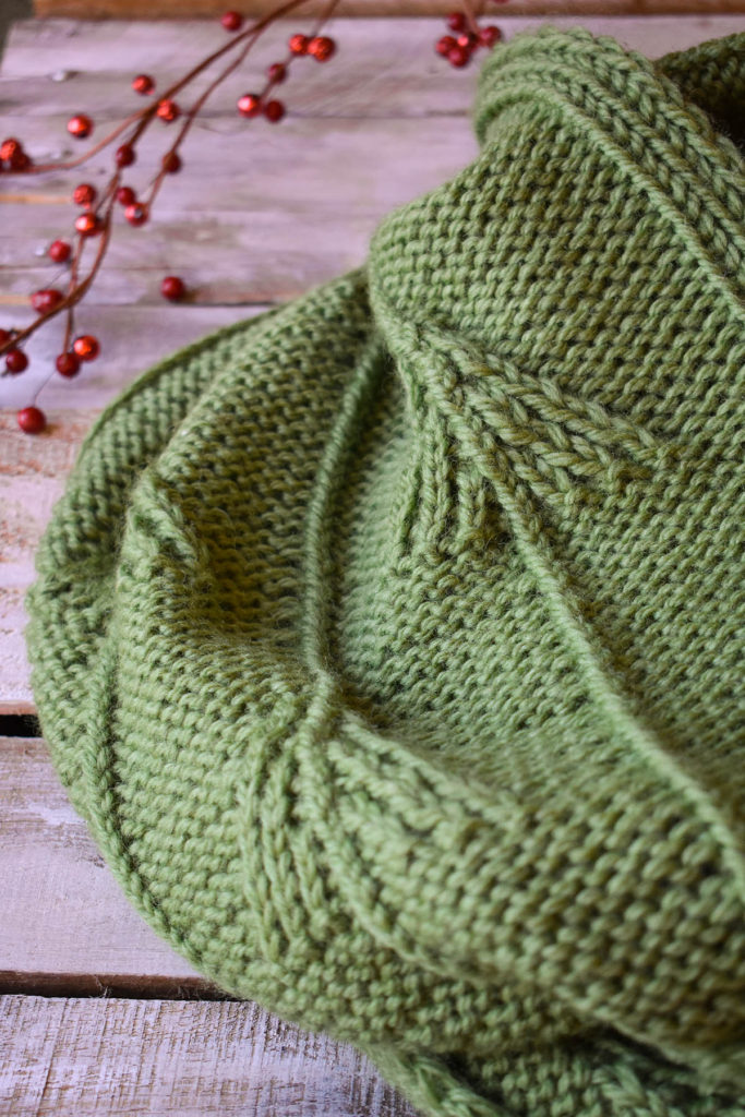 Detail of a green, twisted stitch cowl knit in Universal Yarn Deluxe Chunky.