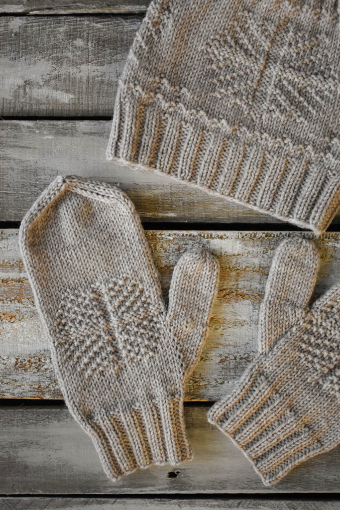 A close-up of a pair of mittens and a hat with a snowflake motif knit in Universal Yarn Deluxe DK Superwash.