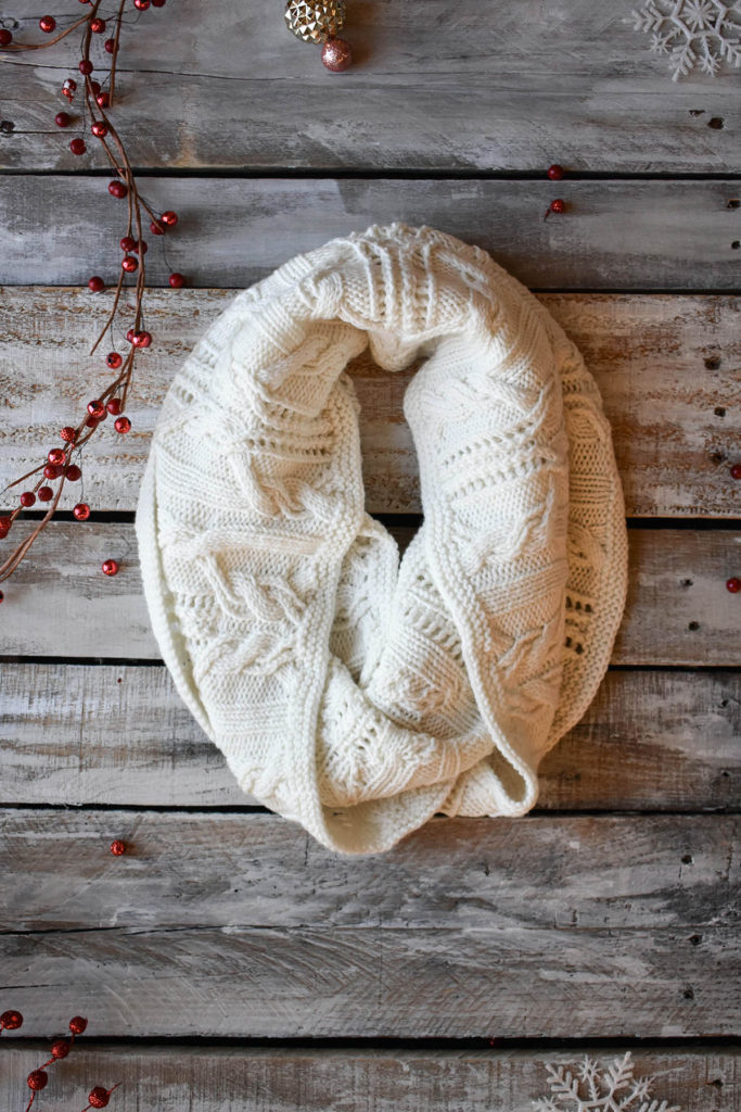 A white cowl featuring cables and lace knit using Fibra Natura Dona.