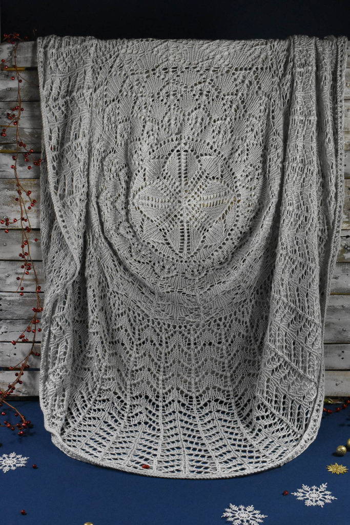 A grey lace blanket draped over a wood palette, knit using Universal Yarn Uptown Worsted. 