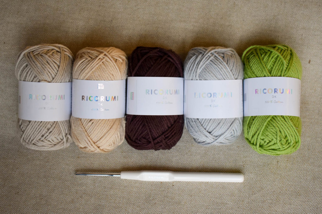 Several skeins of Ricorumi DK yarn in a row, pictured with a crochet hook. 