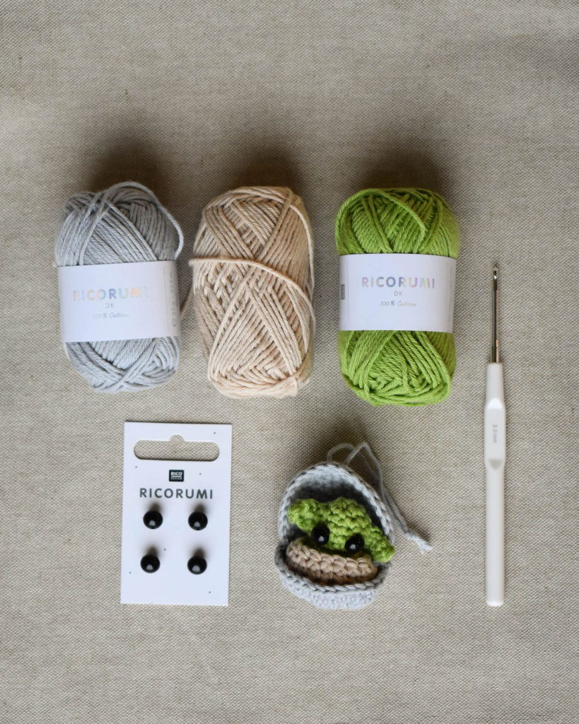 A flat lay of three skeins of Ricorumi yarn, Ricorumi notions, and a small crochet project. 