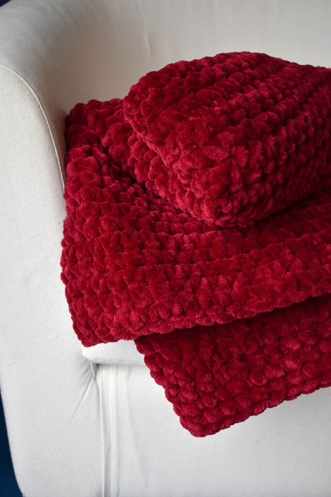 Plush crocheted red blanket folded on upholstered white chair
