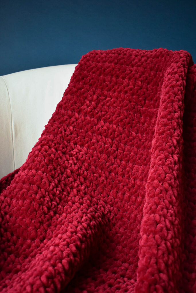 Plush red crocheted throw draped over white chair