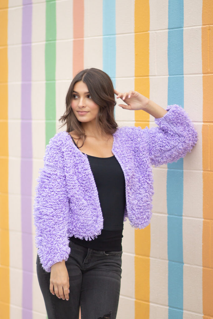 Woman in lavender loop stitch jacket leaning on a wall