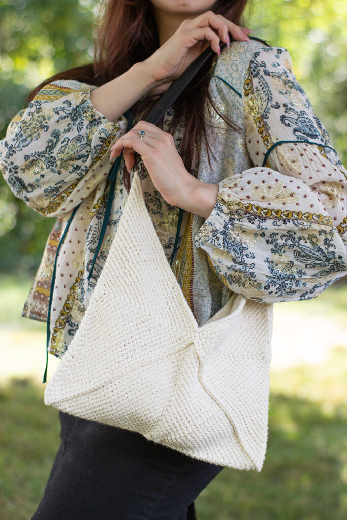 Woman wearing cream-colored crochet handbag slung over shoulder.