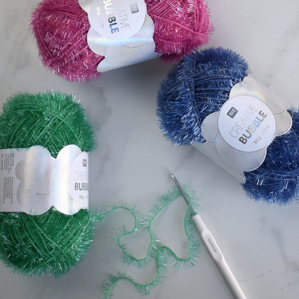 Three skeins of Creative Bubble yarn with a crochet hook