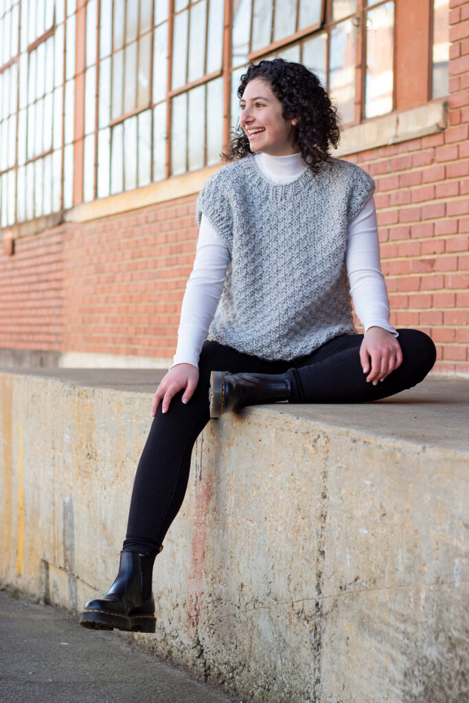 Seated young woman wearing gray knitted vest