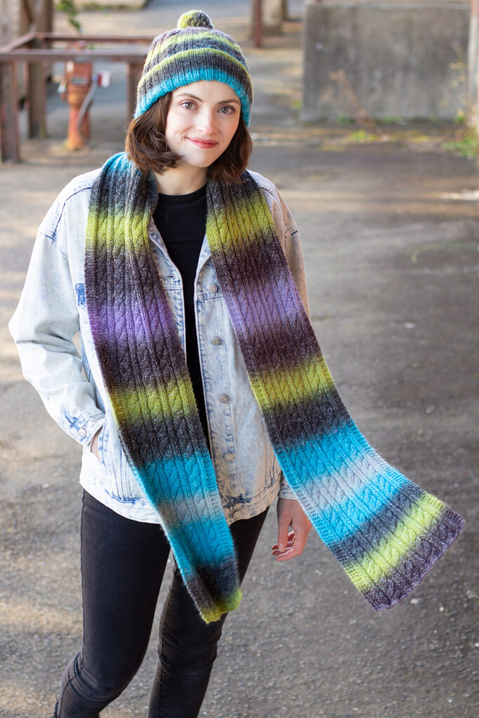 Woman wearing cabled multicolored hat and scarf knitted in Colorburst yarn