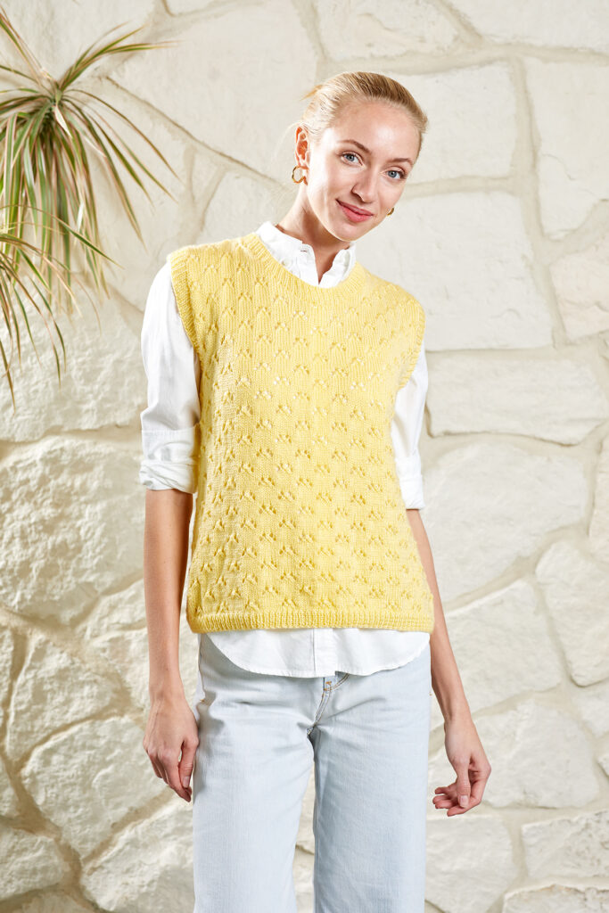 Smiling woman wearing white button-down top and pale yellow vest knitted in Uptown Baby Sport.