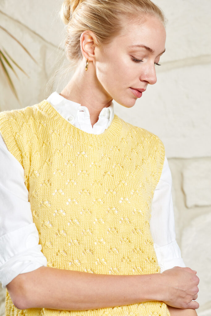 Woman in white blouse with rolled up sleeves, and pale yellow knitted vest.