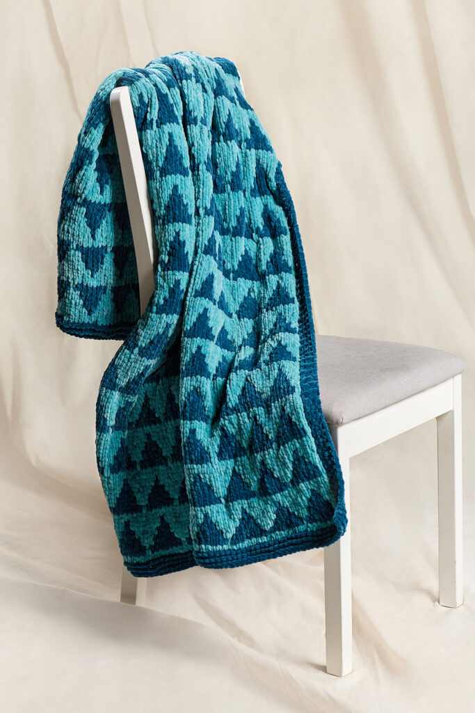 Knitted chenille throw in aqua with triangles motif, draped over a white chair.