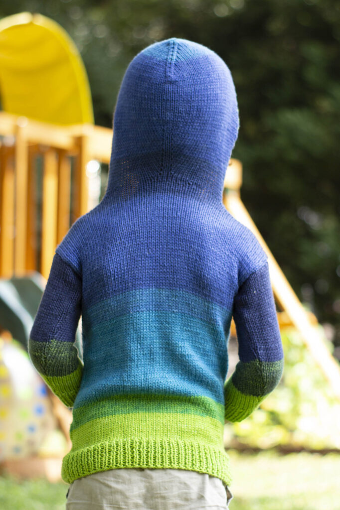 Rear view of boy wearing striped knitted hoodie with the hood up.