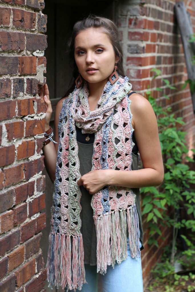 Woman leaning against brick wall and wearing crocheted scarf