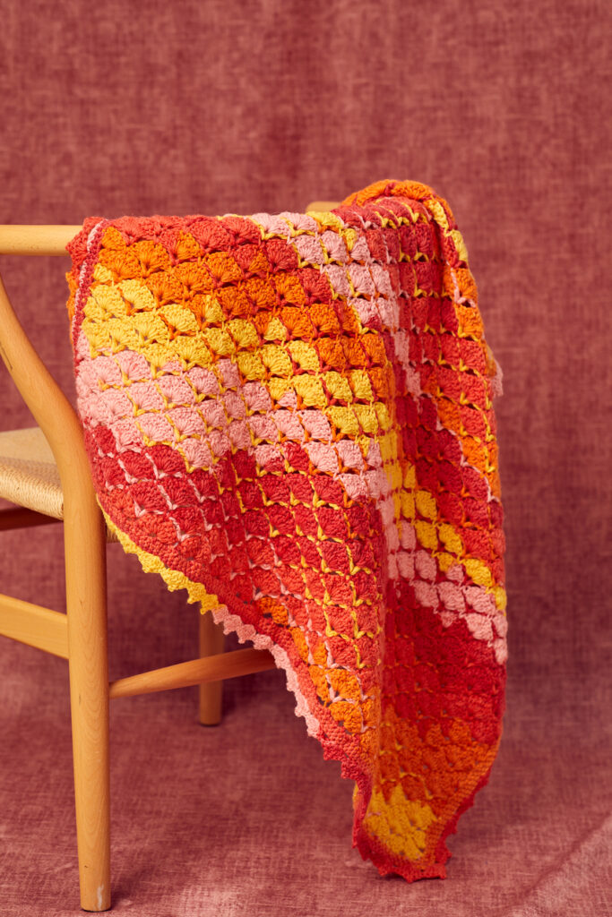 Multicolored crocheted small blanket draped over a chair.