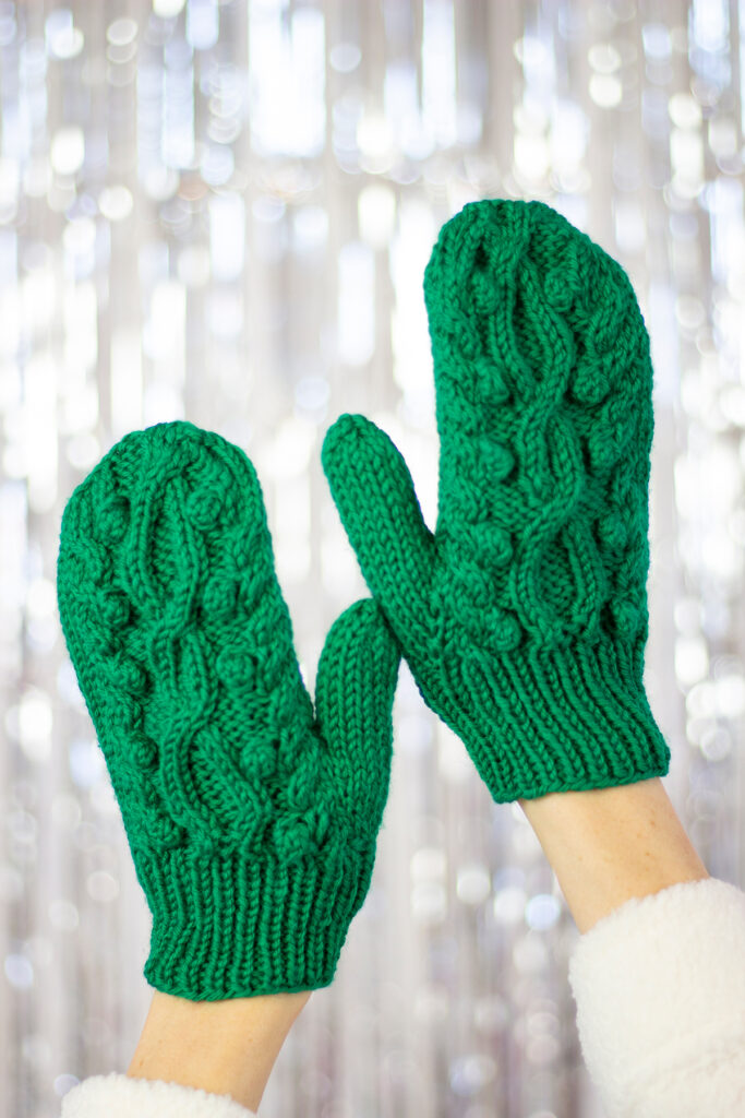 Two hands showing the front of the Hemlock Set mittens, which feature cables and bobbles. 
