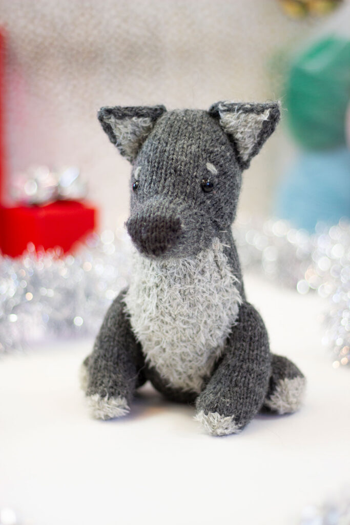 A small hand knitted wolf toy with a fluffy chest, ears, and paws. 