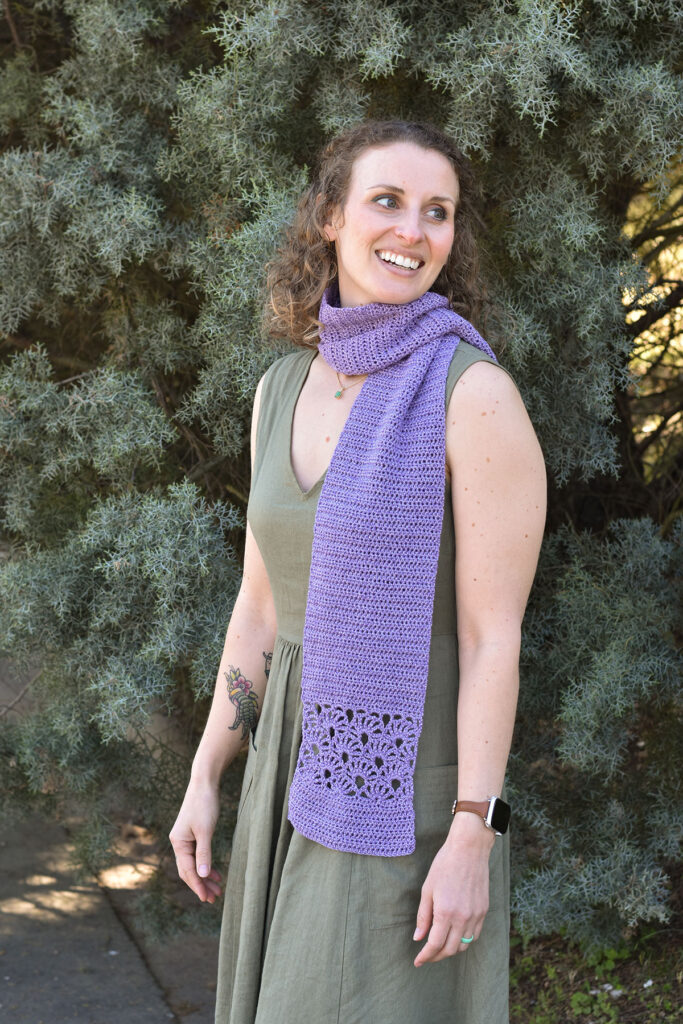 Photo of a person wearing the Tea Leaf Scarf wrapped around their neck with trees in the background.