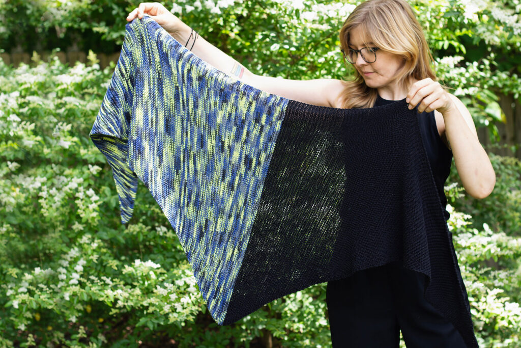 Photo of a person holding the Blur shawl with green plants in the background