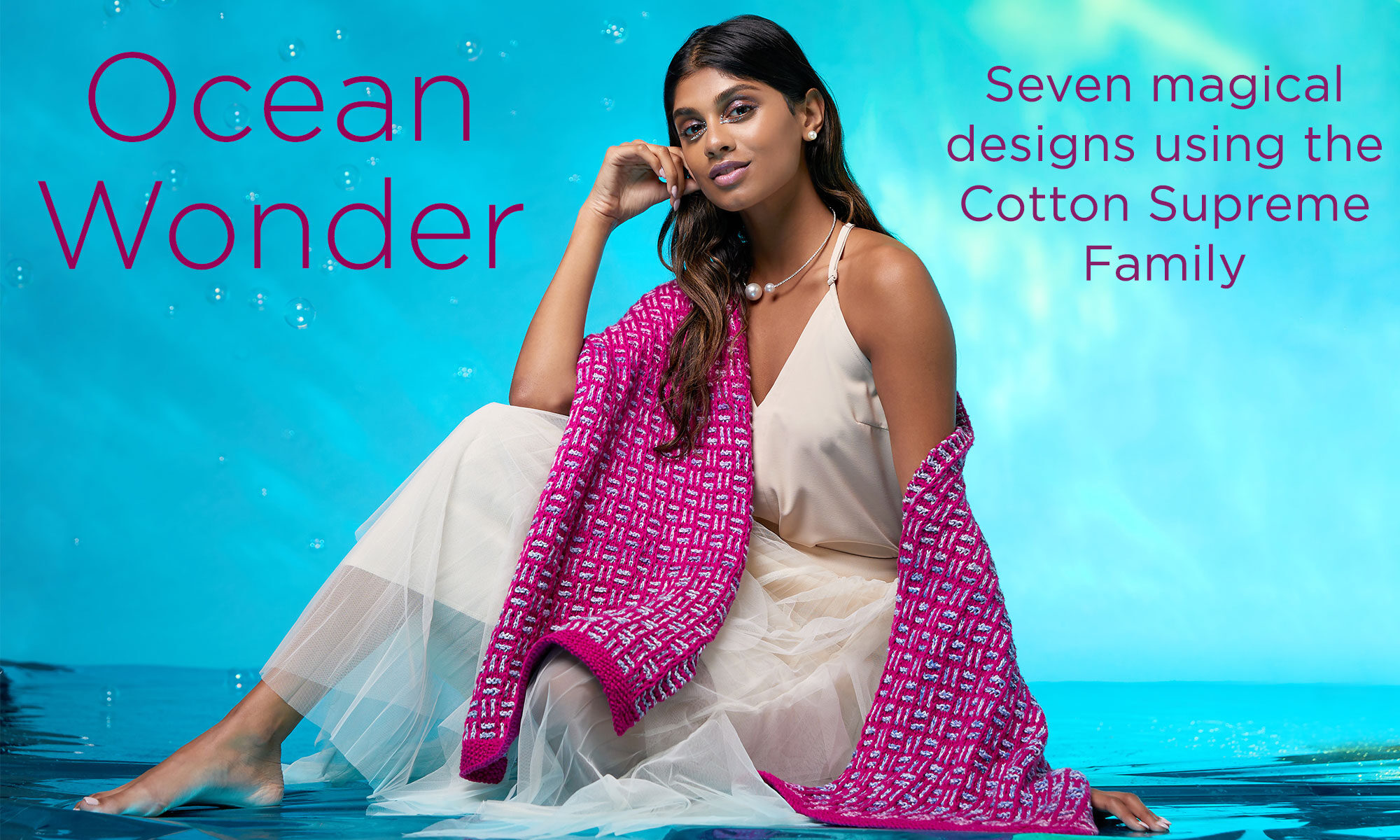 A woman sits wearing a knit wrap from the Ocean Wonder Collection. A description saying there are seven designs in the Cotton Supreme Family is detailed on the right of the image.