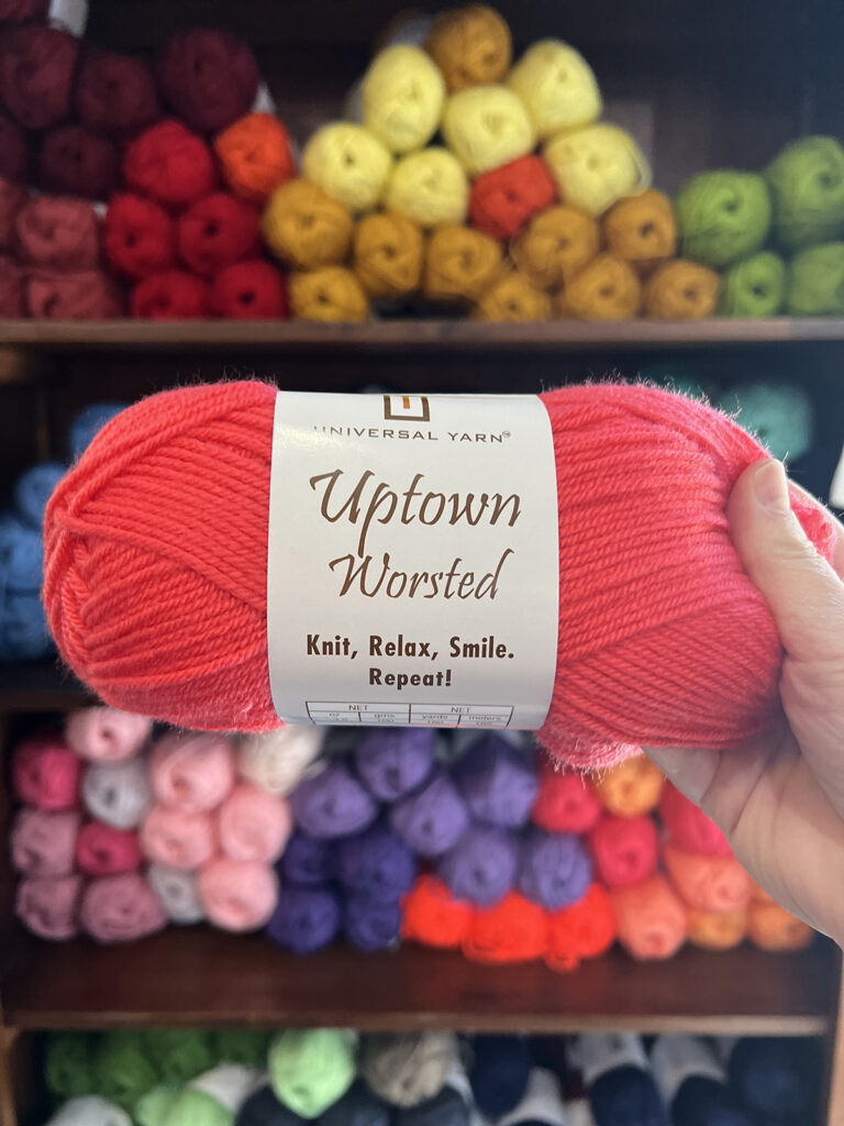 Photo of Uptown Worsted being held with a shelf full of yarn in the background