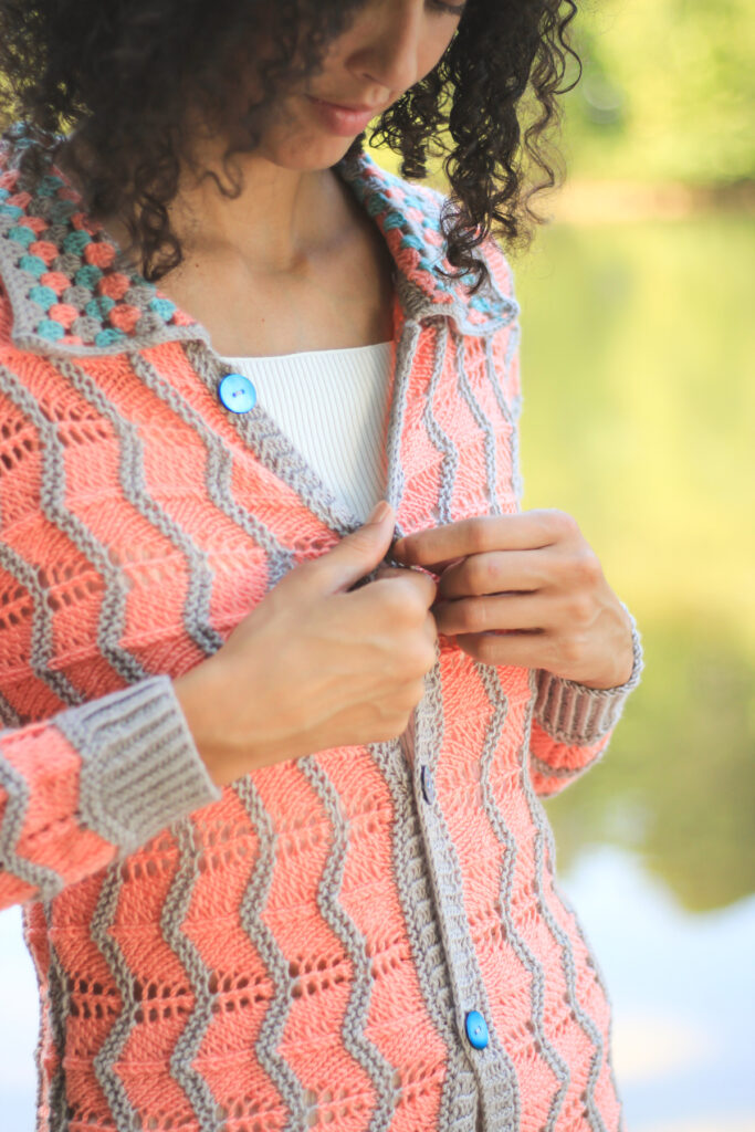 A model carefully buttons the Cattail Cardigan, hand knit and crocheted in Universal Yarn Uptown Bamboo DK. 